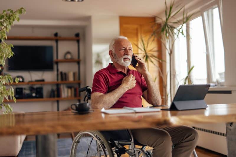 An older, disabled man in a wheelchair talking on the phone. 