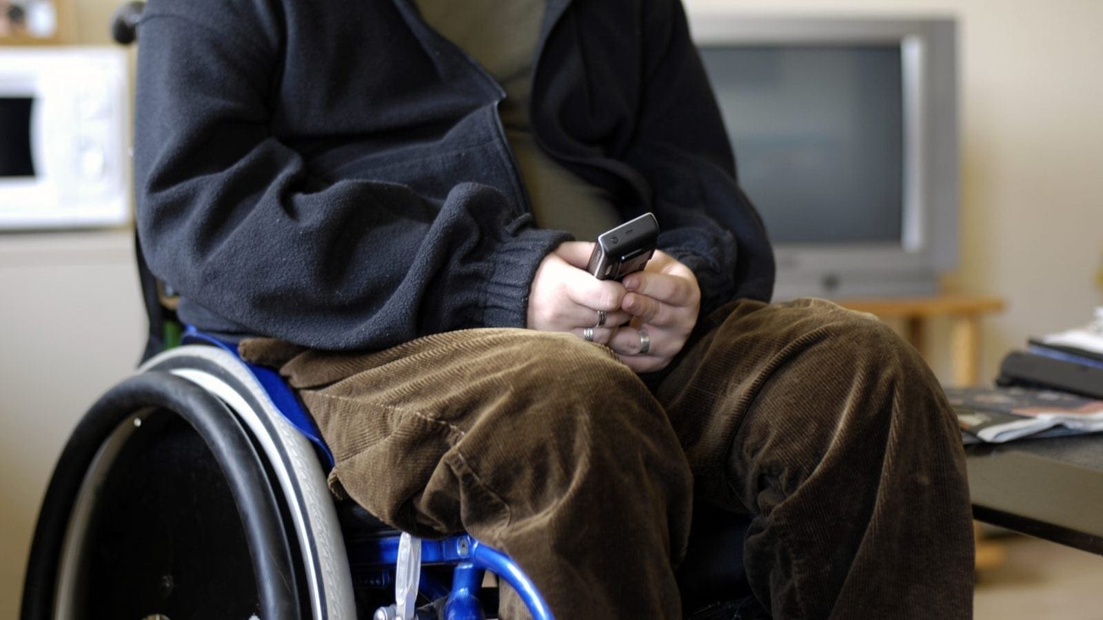 A young man texting on his phone in a wheelchair