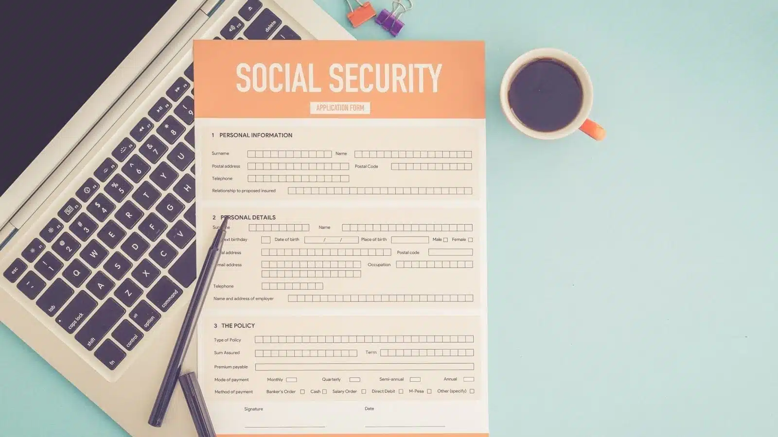 A Social Security application form on top of a laptop, on a desk with a cup of coffee and pens nearby.
