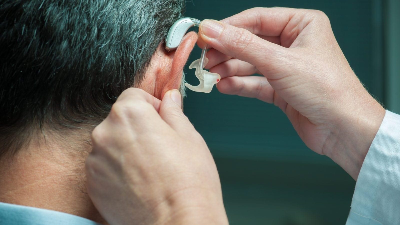 Doctor inserting hearing aid in man's ear